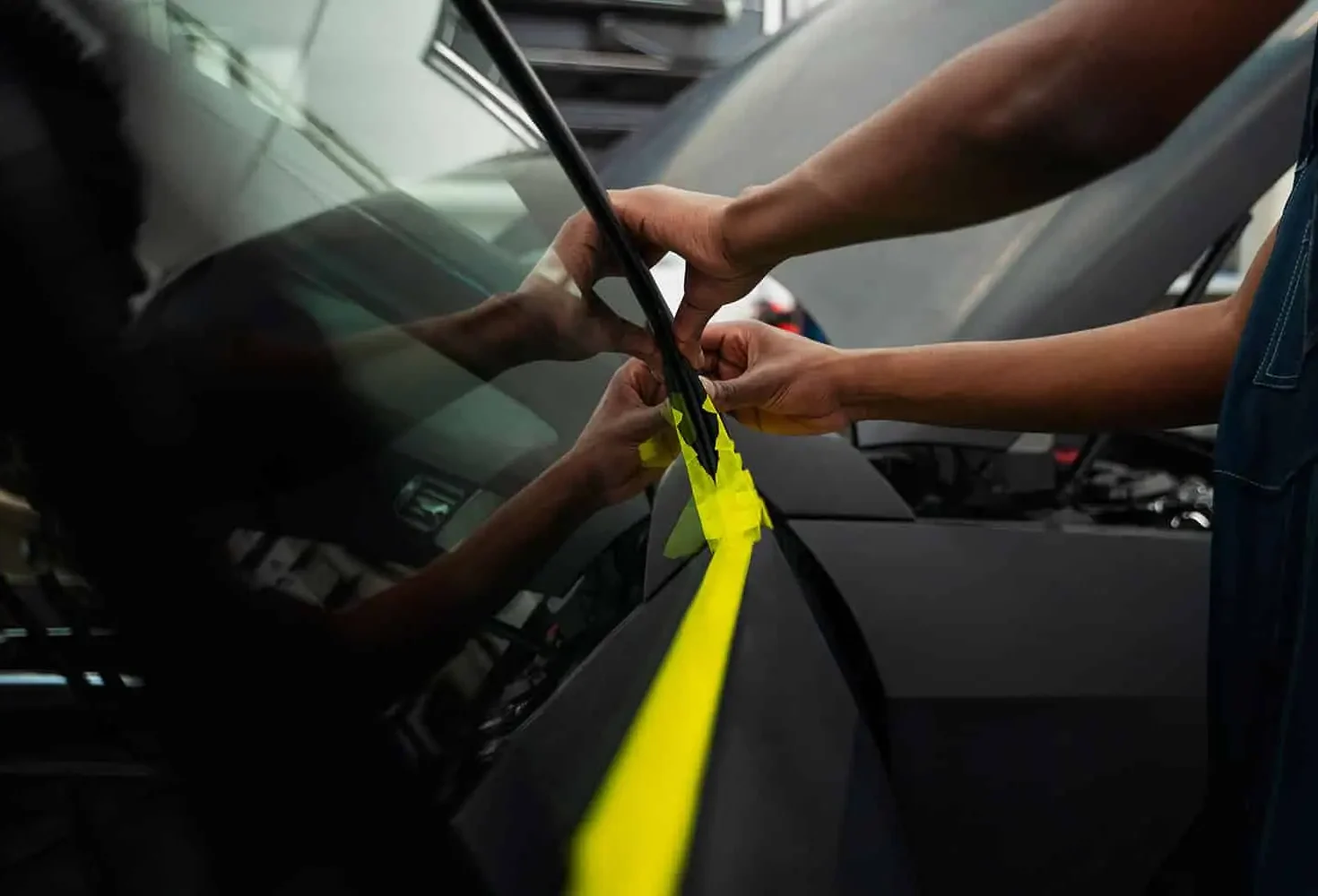 Wraptors Orlando, Vehicle Wraps, PPF & Tint A person applies yellow masking tape in a straight line on the hood of a black car at Wraptors Orlando, with hands and tape reflected on the car’s surface—a meticulous step often seen during PPF or Orlando Florida Car Wraps installations. Orlando, FL