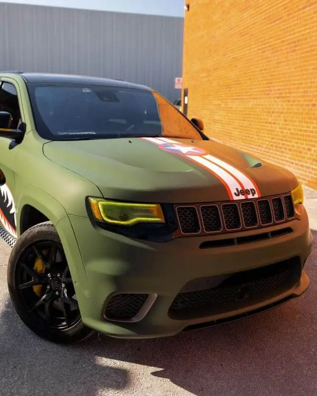 Wraptors Orlando, Vehicle Wraps, PPF & Tint Green Jeep SUV with a shark mouth decal on the side and yellow-tinted headlights, parked next to a brick wall—a bold example of creativity by Wraptors Orlando, your go-to source for Orlando Florida Car Wraps and premium PPF protection. Orlando, FL