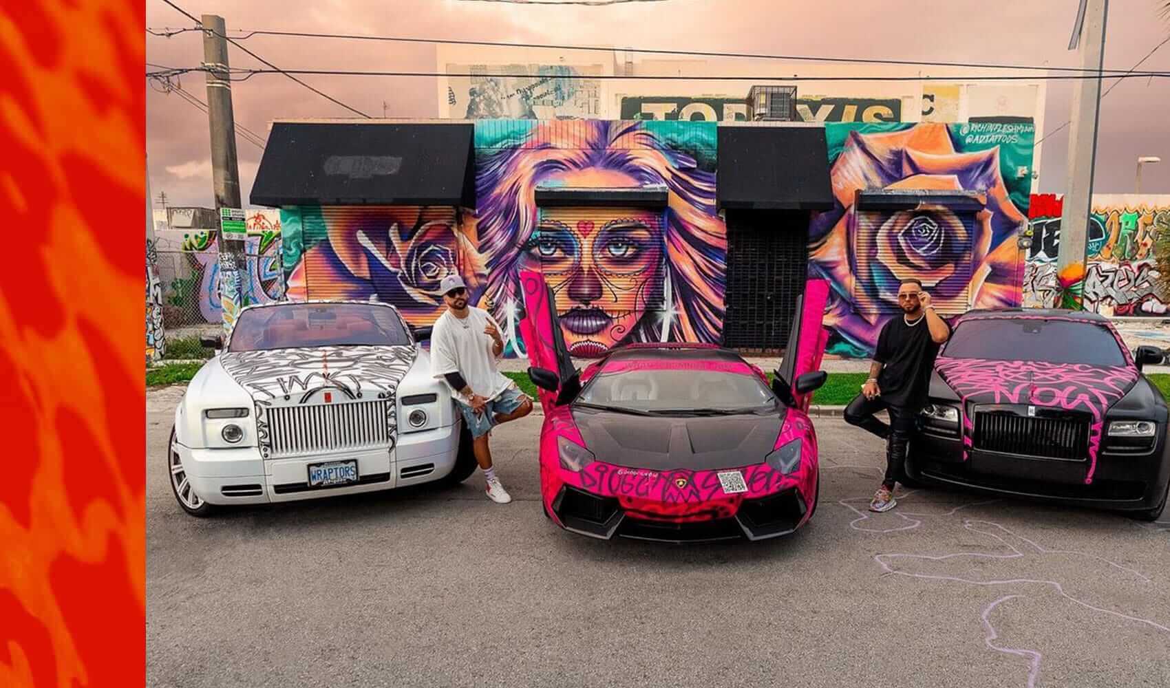 Wraptors Orlando, Vehicle Wraps, PPF & Tint Two people pose with a pink Lamborghini and two white cars, all featuring eye-catching graffiti-style Orlando Florida Car Wraps by Wraptors Orlando, in front of a colorful mural of a woman's face and flowers. Orlando, FL
