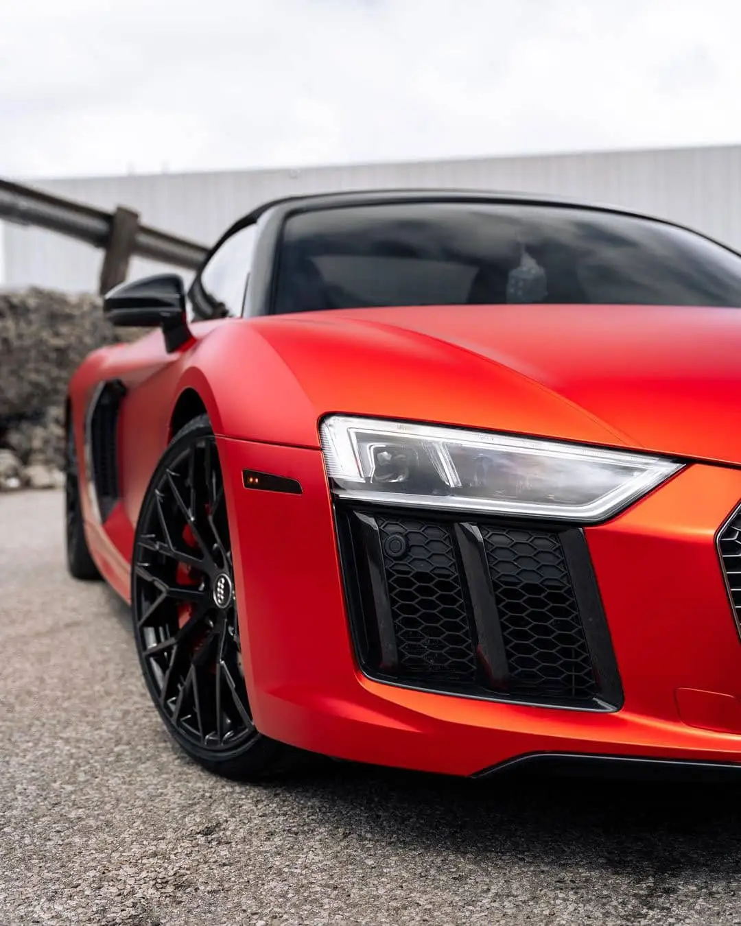 Wraptors Orlando, Vehicle Wraps, PPF & Tint A close-up view of the front left side of a red Audi R8 sports car parked on a paved surface, showing the headlight, wheel, and grille—all expertly protected with PPF by Wraptors Orlando, a leading name in Orlando Florida Car Wraps. Orlando, FL