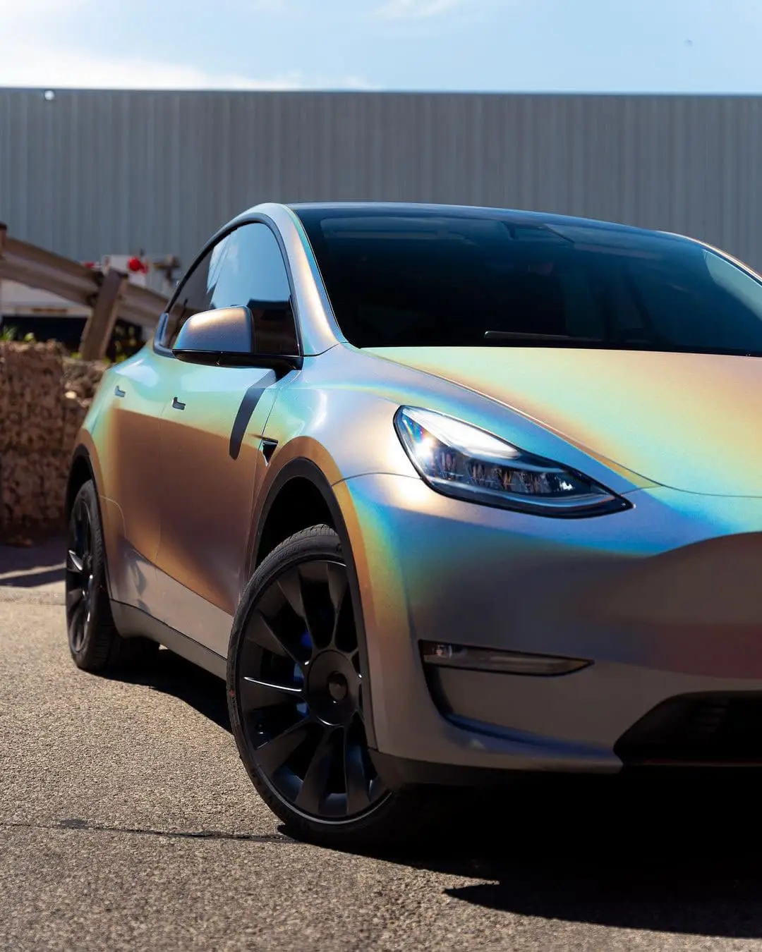 Wraptors Orlando, Vehicle Wraps, PPF & Tint A matte iridescent-colored Tesla Model Y featuring premium PPF by Wraptors Orlando is parked outdoors on a sunny day, with part of a building visible in the background—highlighting the craftsmanship of Orlando Florida Car Wraps. Orlando, FL