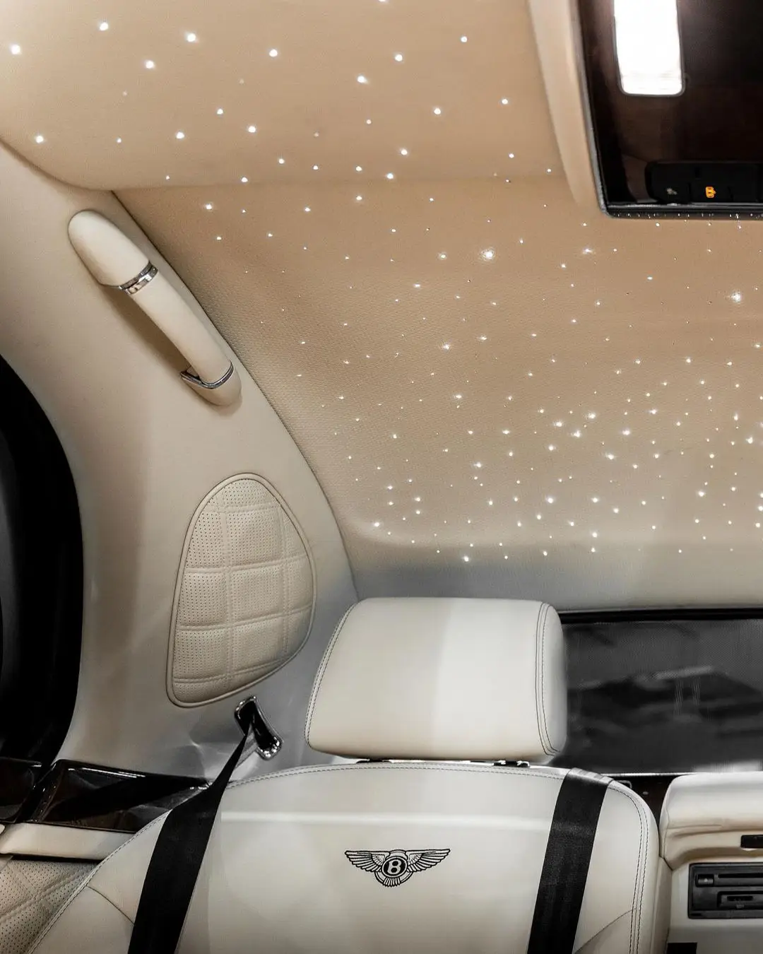 Wraptors Orlando, Vehicle Wraps, PPF & Tint Cream-colored luxury car interior with embroidered seat logo, seatbelt, and ceiling featuring small LED star-like lights—expertly customized by Wraptors Orlando, your trusted source for Orlando Florida Car Wraps and premium PPF services. Orlando, FL