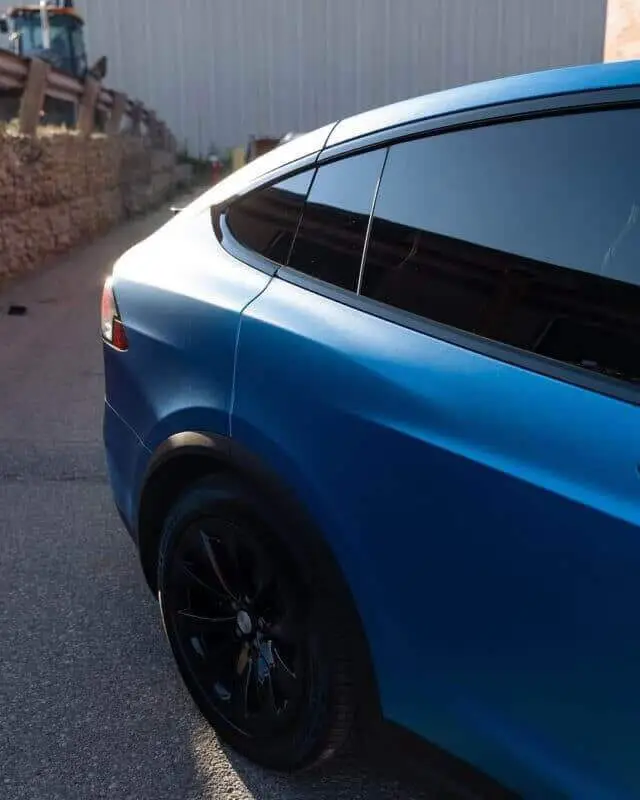 Wraptors Orlando, Vehicle Wraps, PPF & Tint A blue car with tinted windows and black wheels is parked on a paved surface near a stone wall and a building, showcasing the expert finish of Wraptors Orlando—leaders in Orlando Florida Car Wraps. Orlando, FL